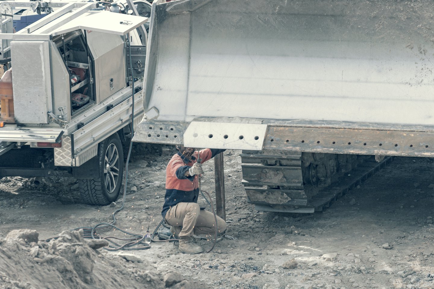 Welder working on heavy machinery blade outdoors.