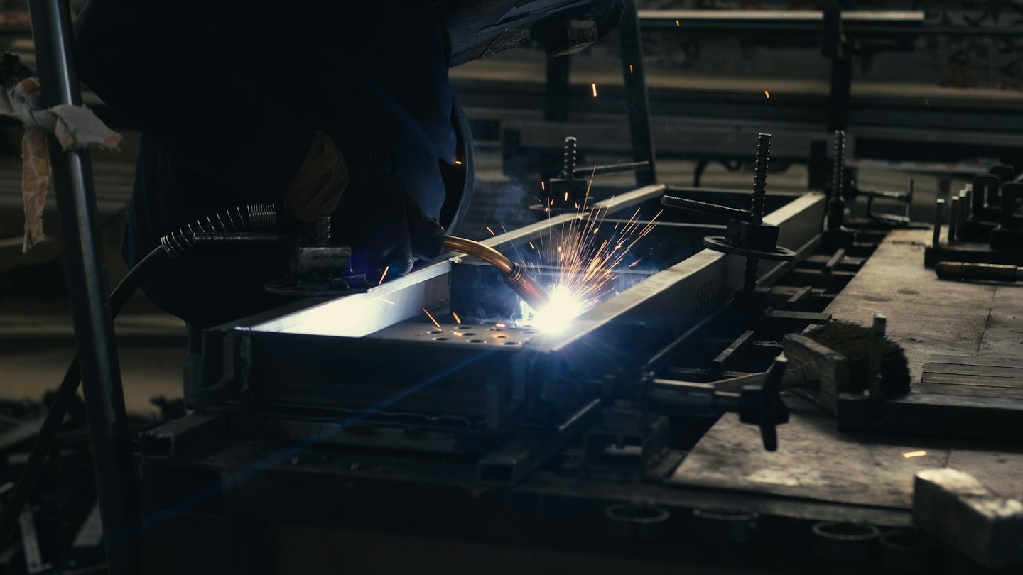 Worker welds metal in a workshop creating sparks.