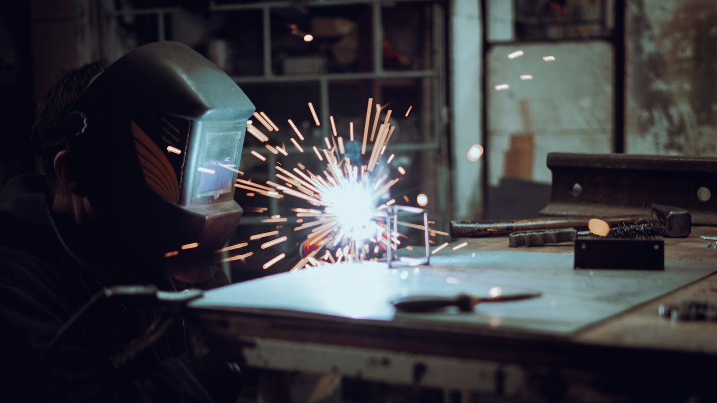 Welder with bright sparks in a dark workshop.