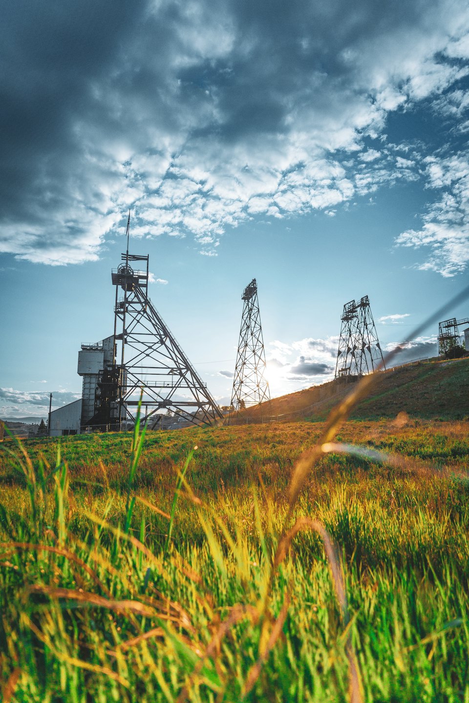 Large industrial metal structures stand on a grassy hillside.