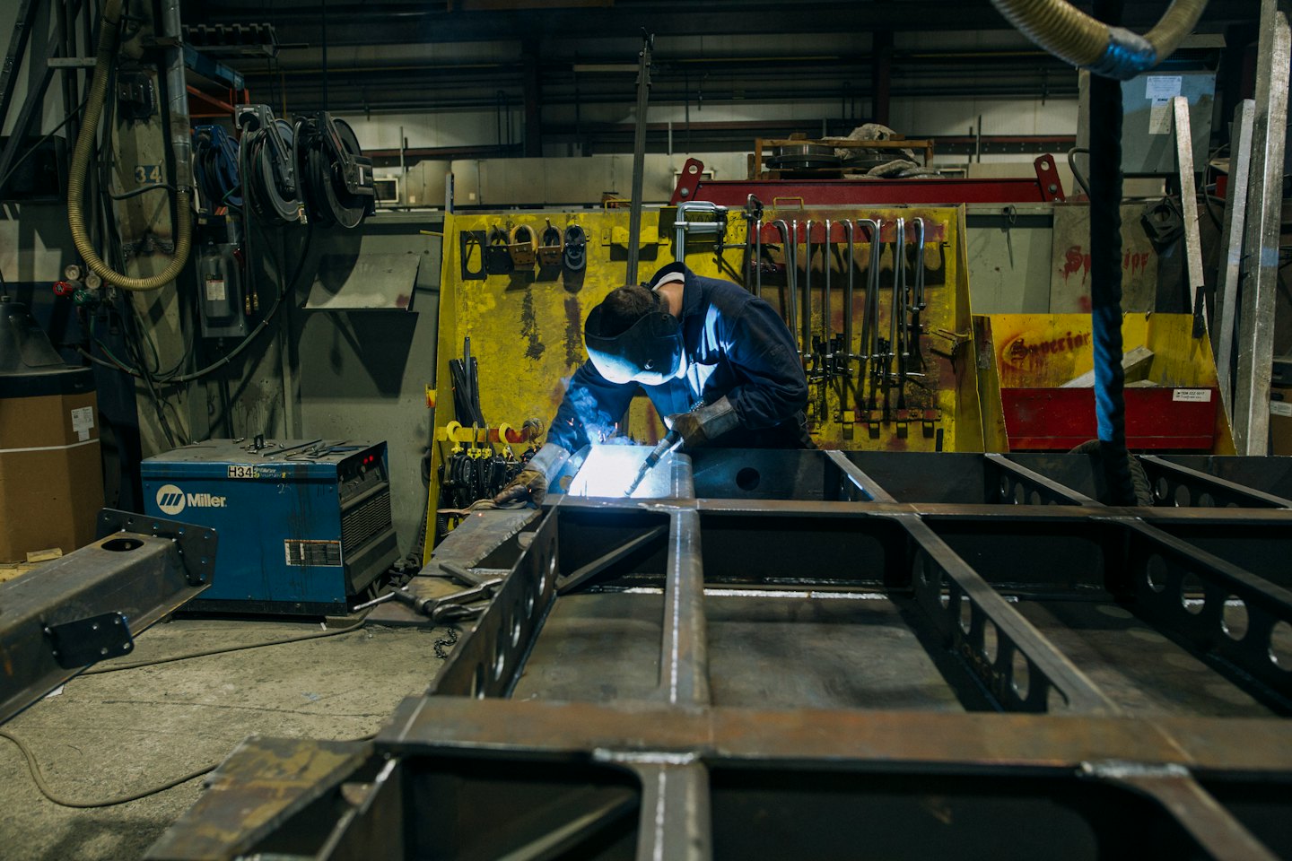 Welder in helmet and gloves sparks metal frame in workshop.