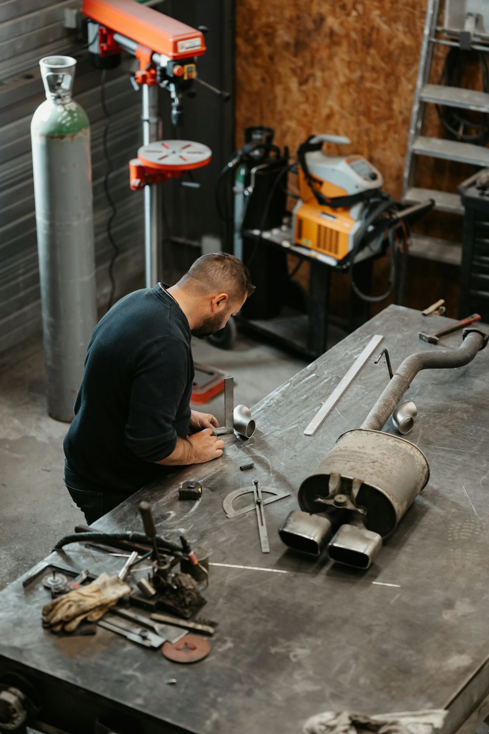 Fabricator shaping metal parts on a steel workbench in a workshop.
