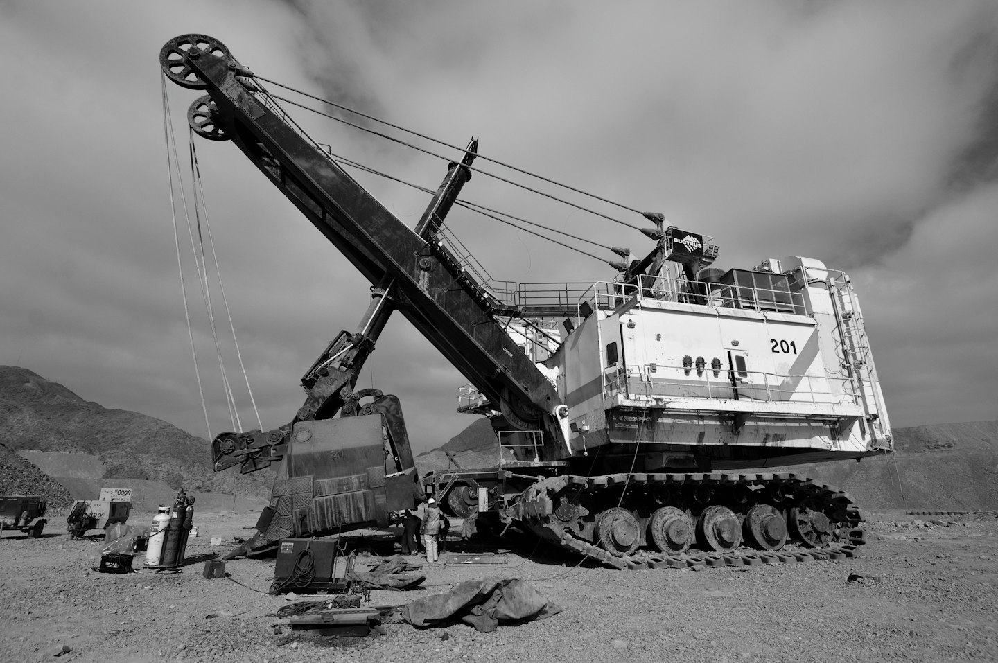 Workers perform maintenance on a large rope shovel in a mine.