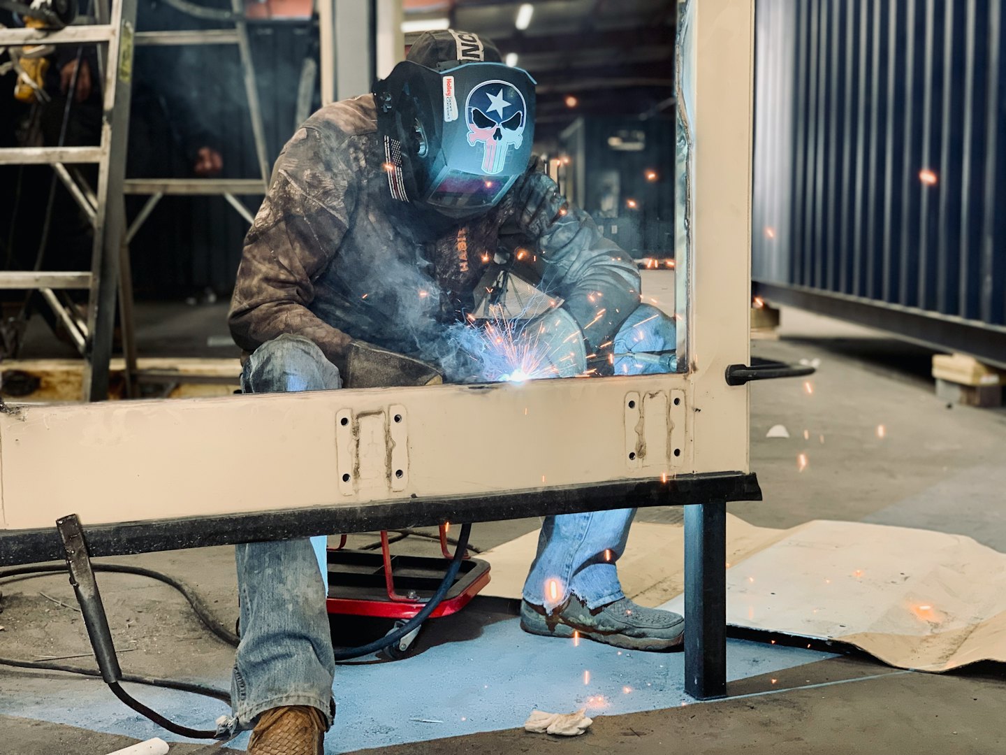 Welder in mask sparks metal frame in workshop.