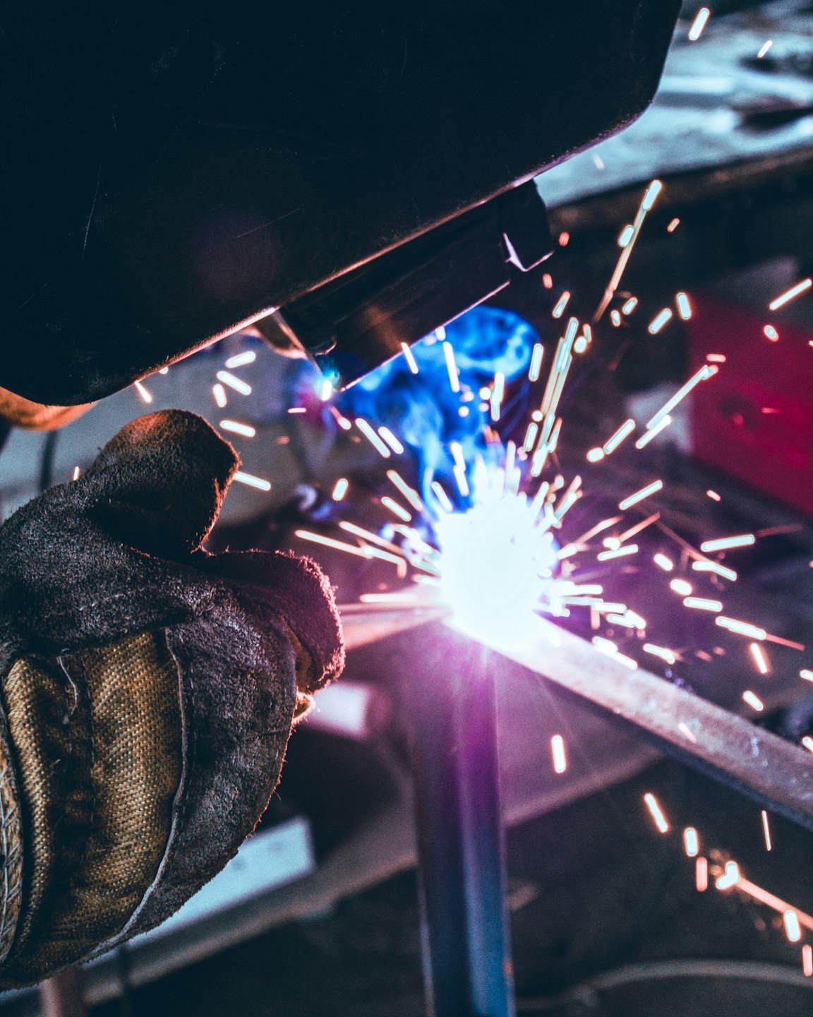 Welder in helmet and glove welding metal with sparks flying.