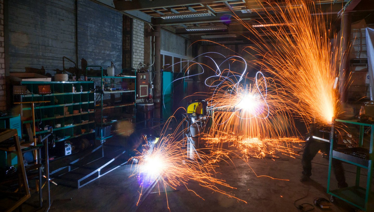 Welder in protective gear creating sparks in a workshop.
