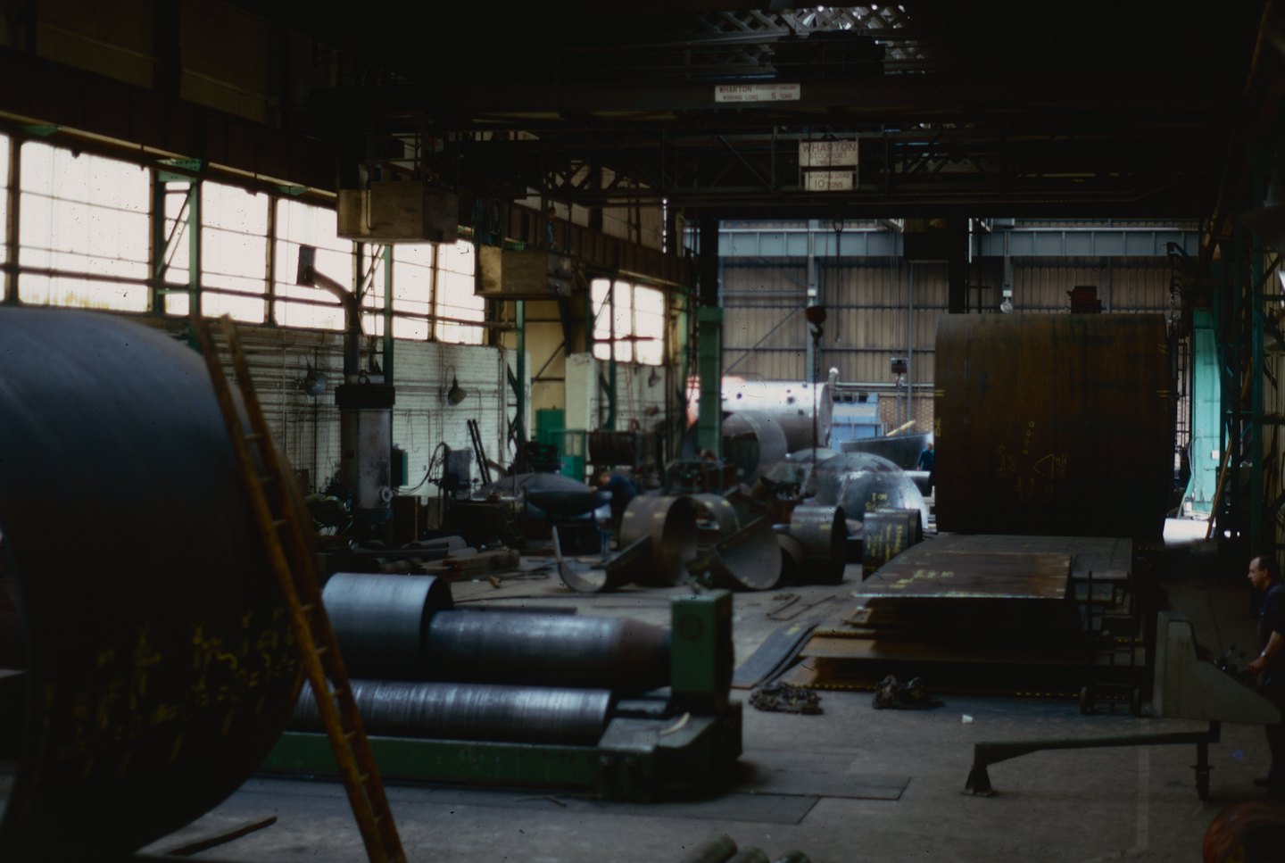 Man operating heavy machinery in a large, dimly lit workshop.