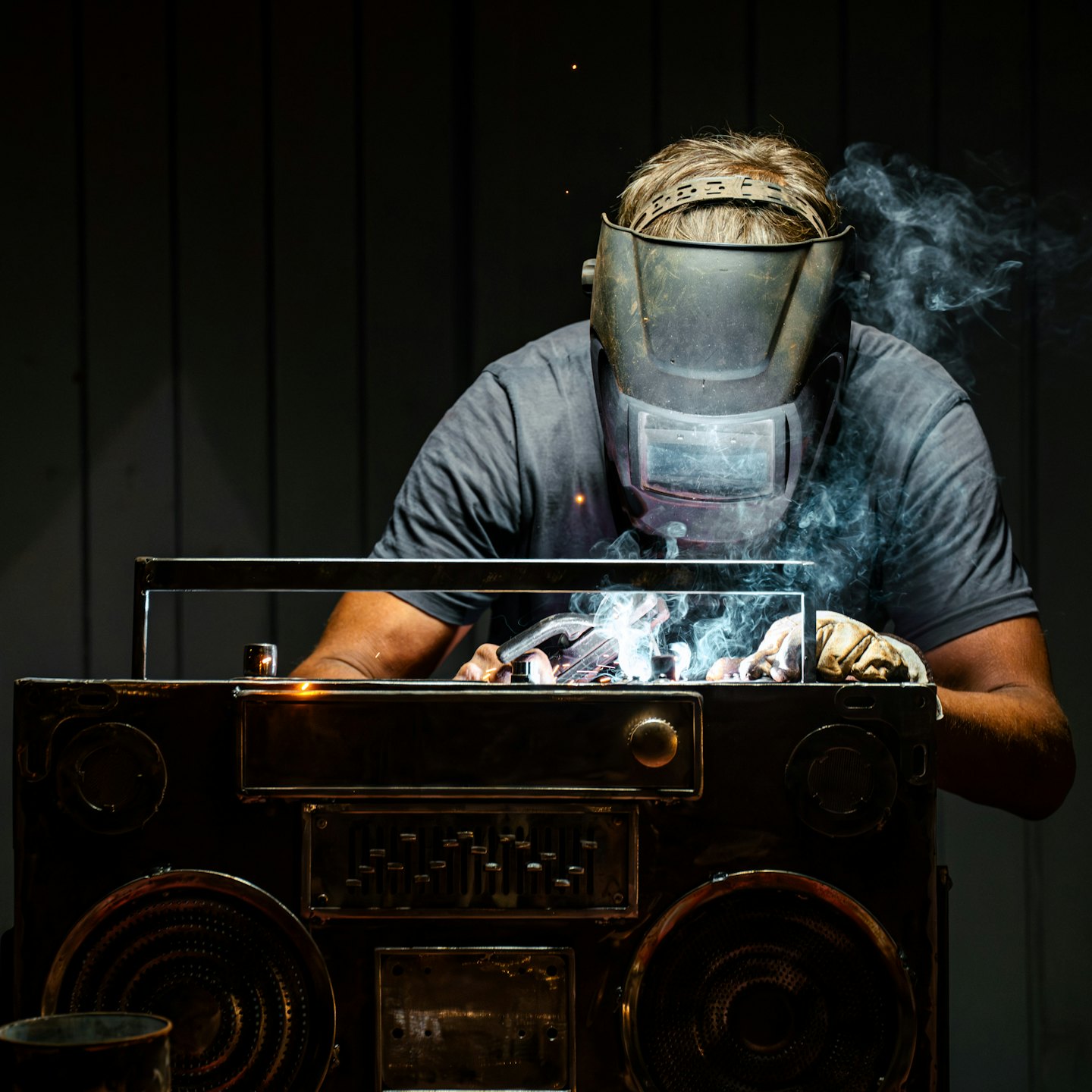Welder in mask and gloves creates a metal boombox structure.